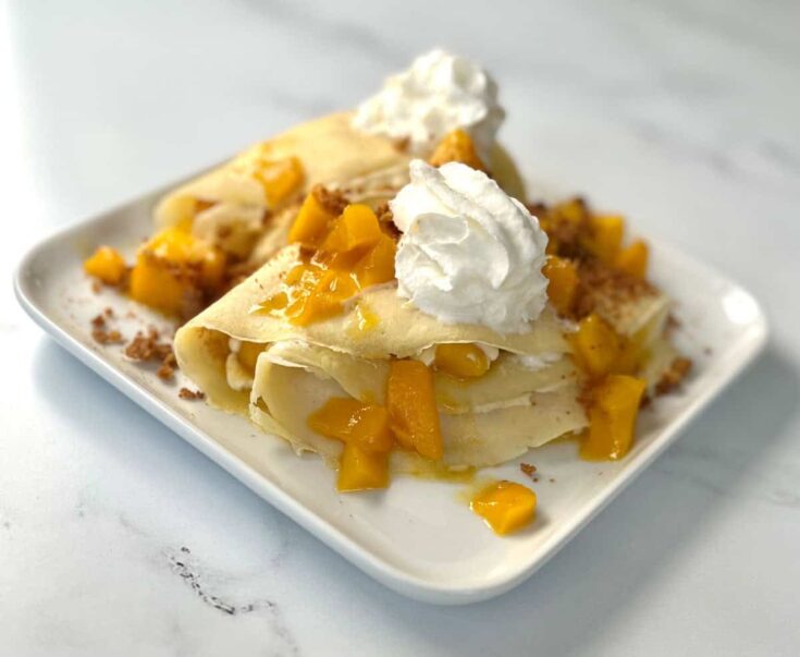 A plate with crepes topped with mango and whipped cream.