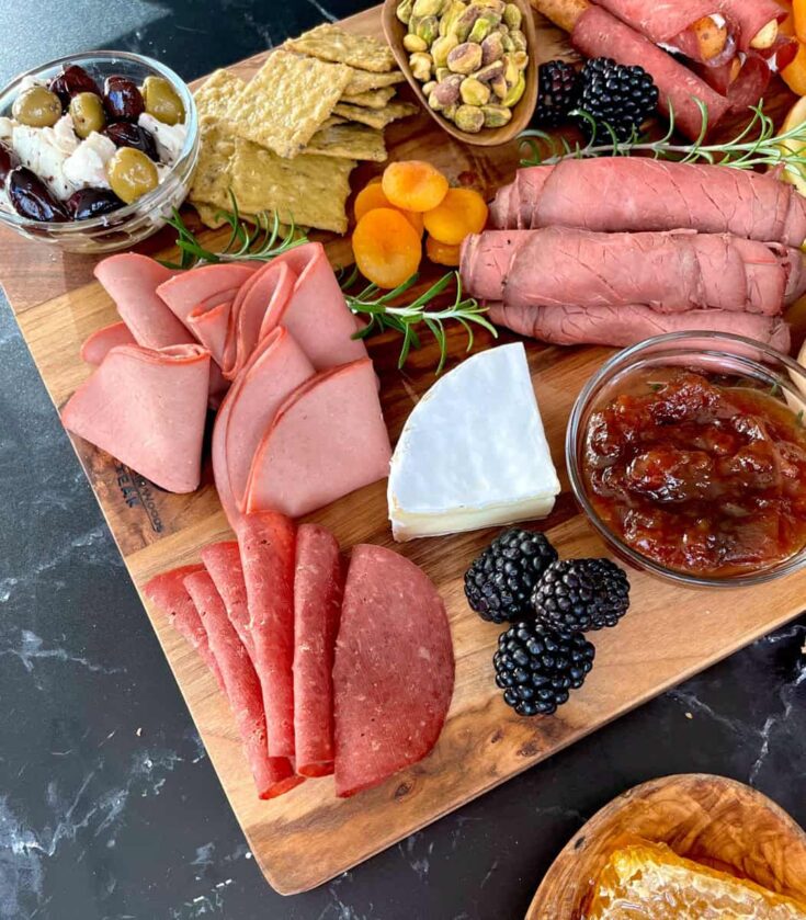 A meat and cheese platter with crackers, fruit, and other snacks.