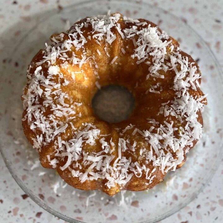 A bundt cake with shredded coconut on a glass plate.