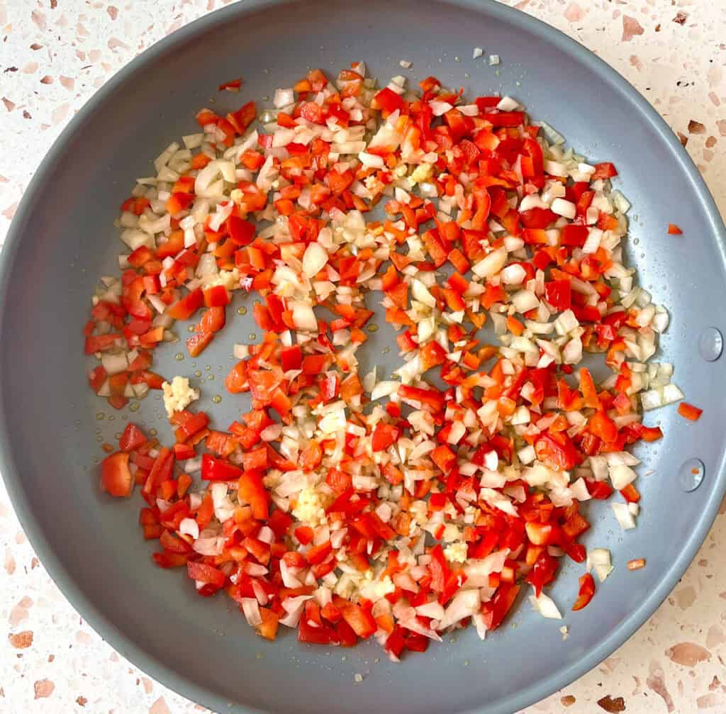 A pan filled with chopped red peppers, onions, and garlic.