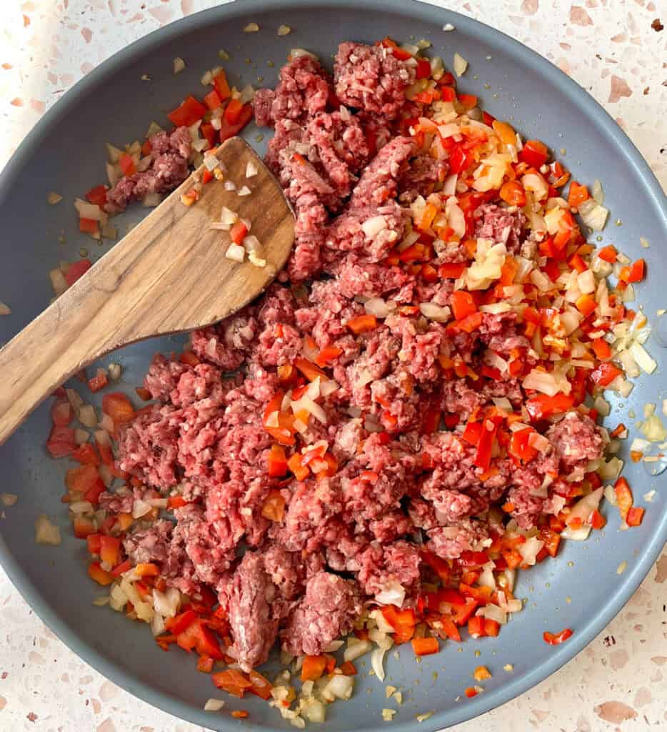A skillet with ground beef, onions, and peppers cooking.