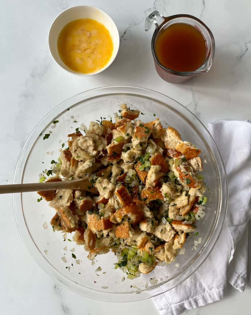 A clear bowl of stuffing and vegetables with a wooden spoon.