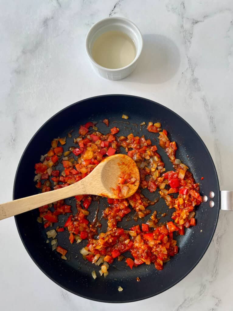A pan with red peppers and onions cooking in it.