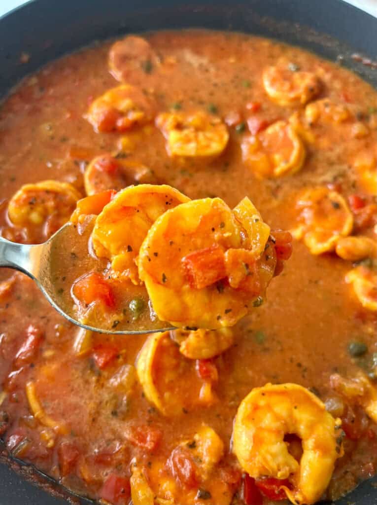 A spoonful of shrimp and tomato sauce in a skillet.