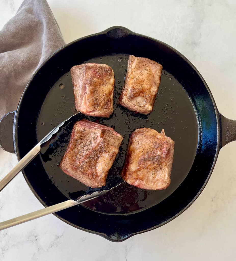 Four pieces of meat in a cast iron skillet.