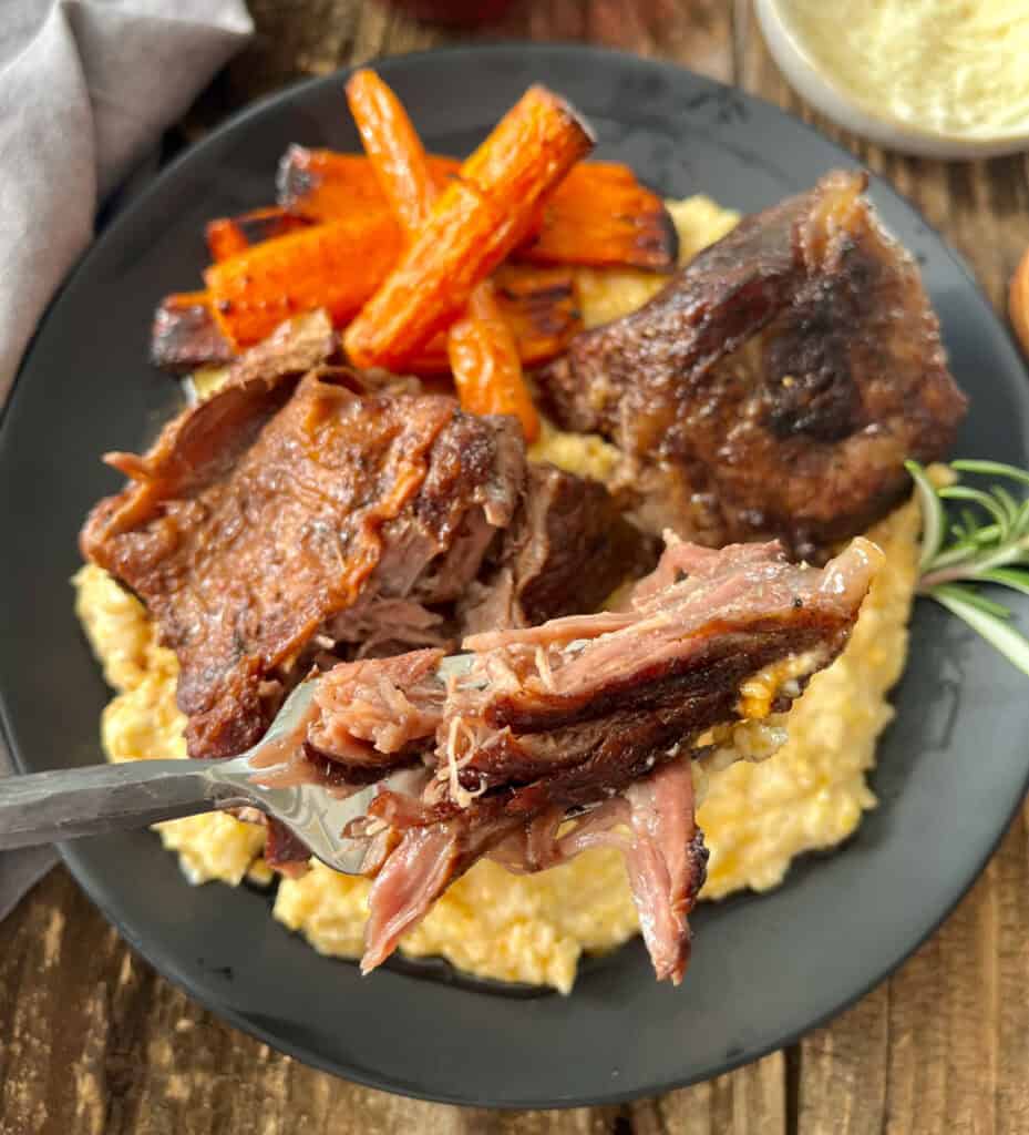 A fork is lifting up a piece of meat from a plate of polenta.