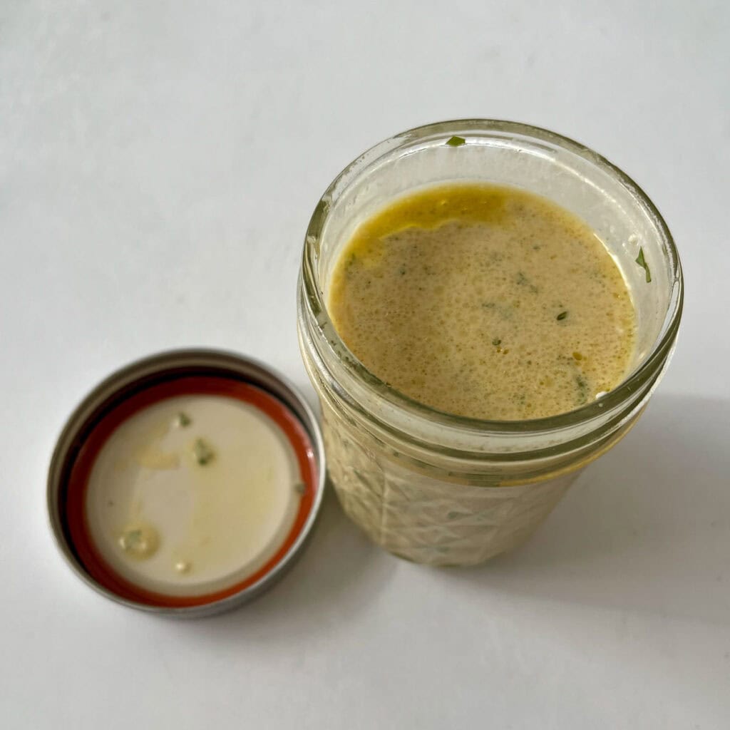 A jar of dressing with a lid next to it on a white counter.