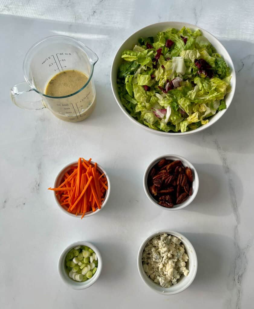 The ingredients for a salad are in bowls on a counter.