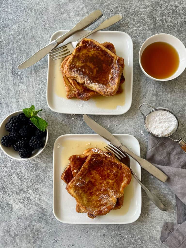 Two white plates with french toast with maple syrup and blackberries.