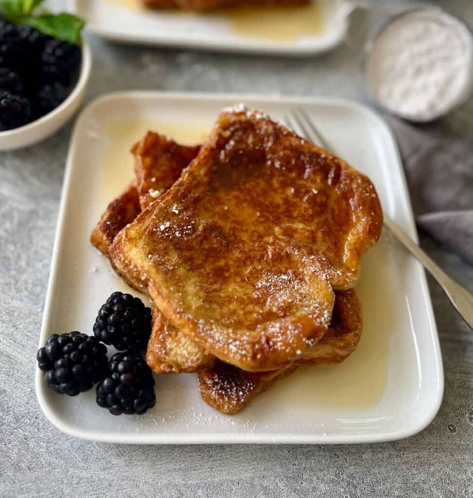 French toast with syrup and blackberries on a white plate.