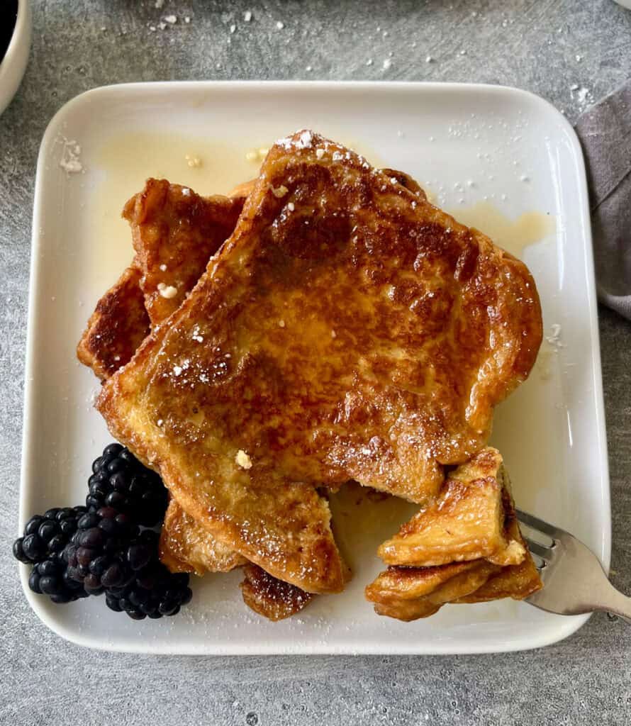 French toast with syrup and berries on a white plate.