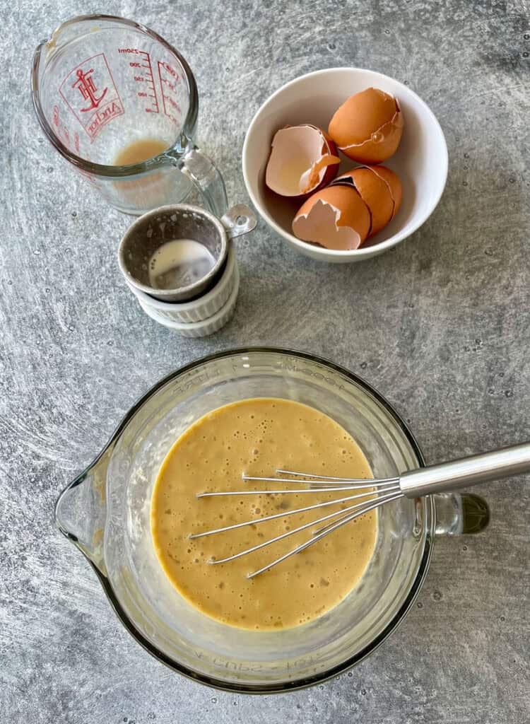 Eggs, whisk, and other ingredients in a bowl.