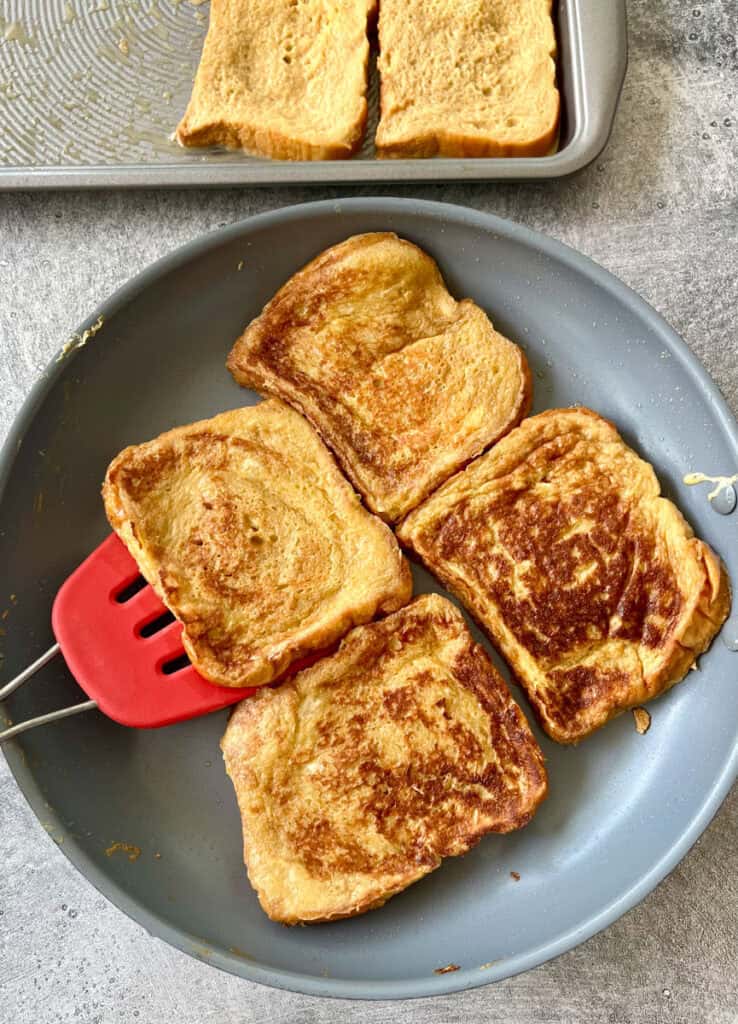Four slices of french toast in a pan with a spatula.