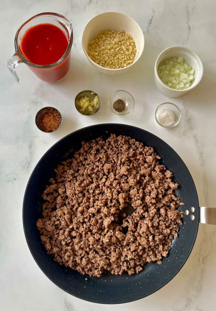 Ingredients for the beef mixture of a cheeseburger pie in a frying pan.
