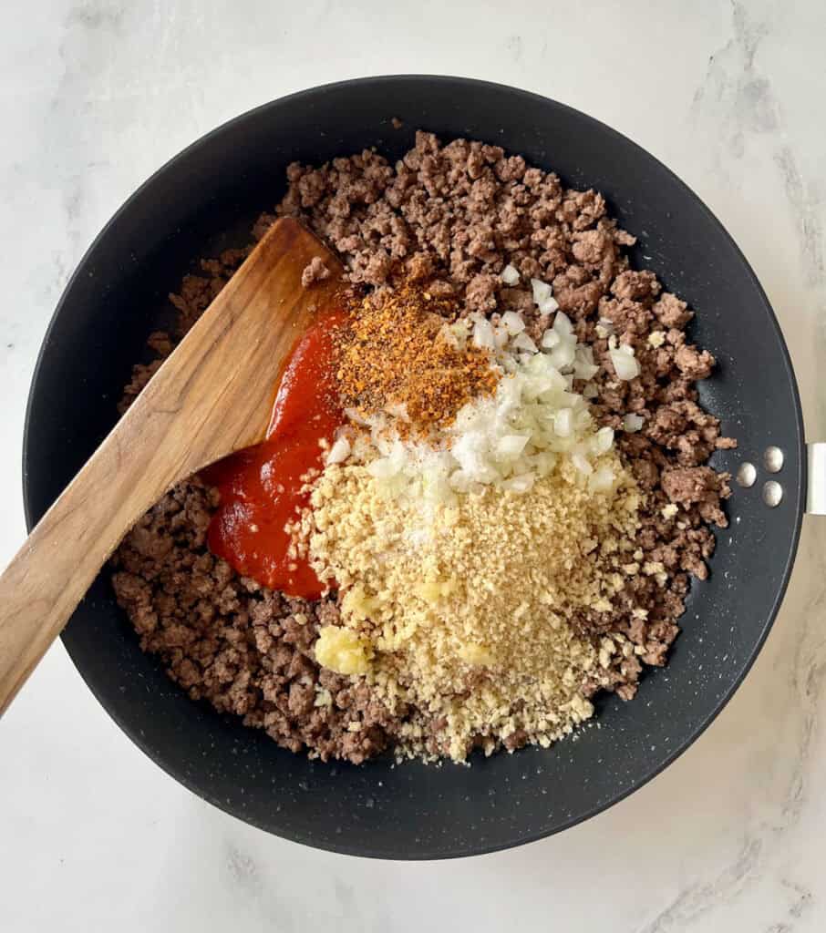 Ground beef, onion, and spices in a frying pan.