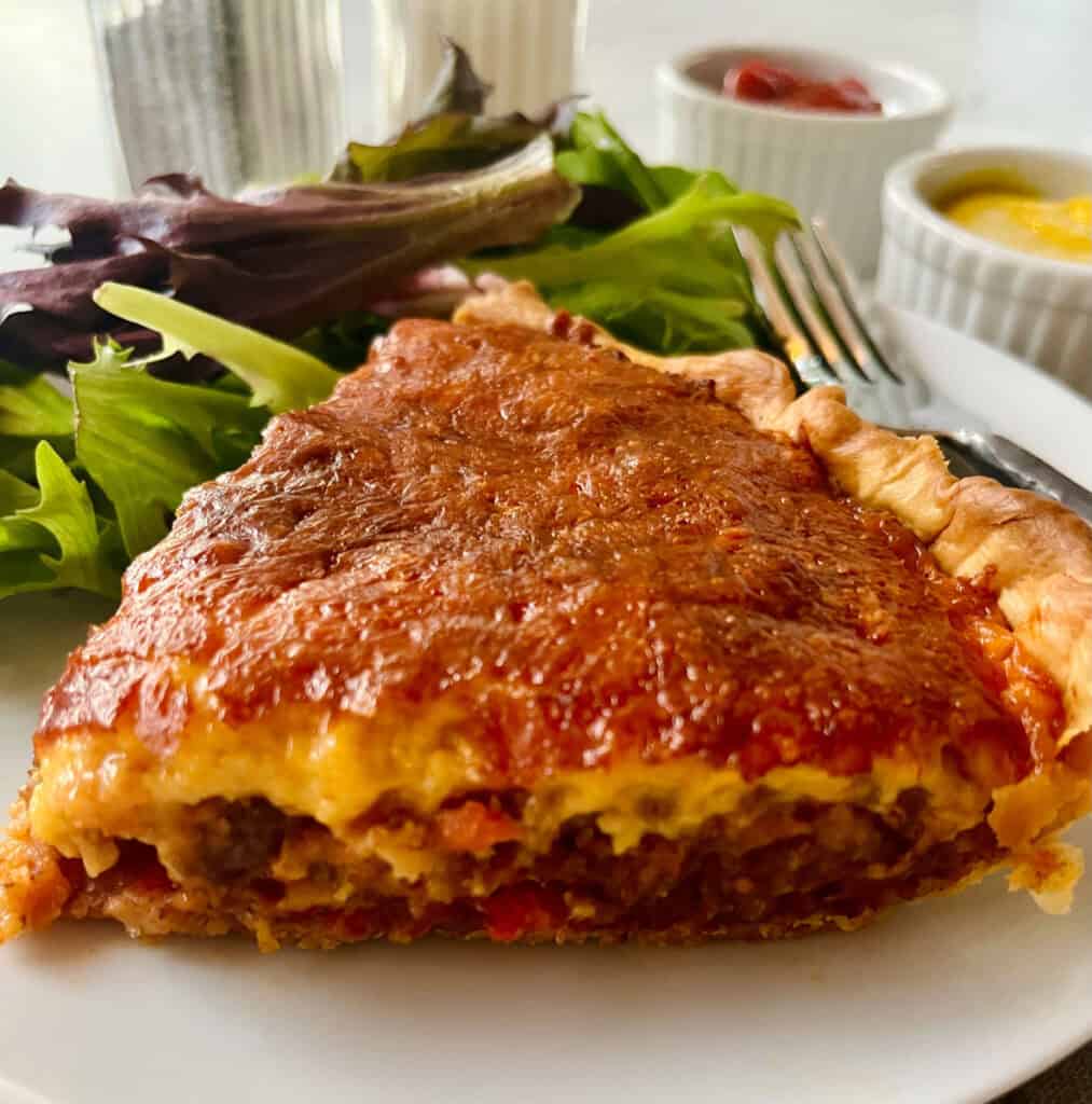 A slice of pie on a plate with a salad.