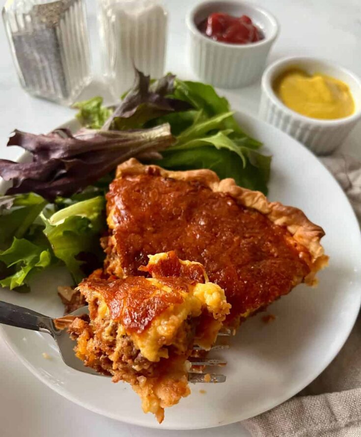 Cheeseburger pie and salad greens on a white plate.