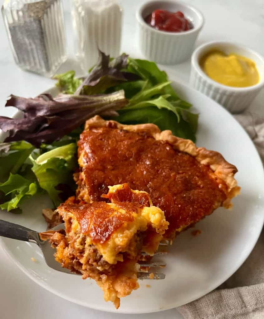 Cheeseburger pie and salad greens on a white plate.