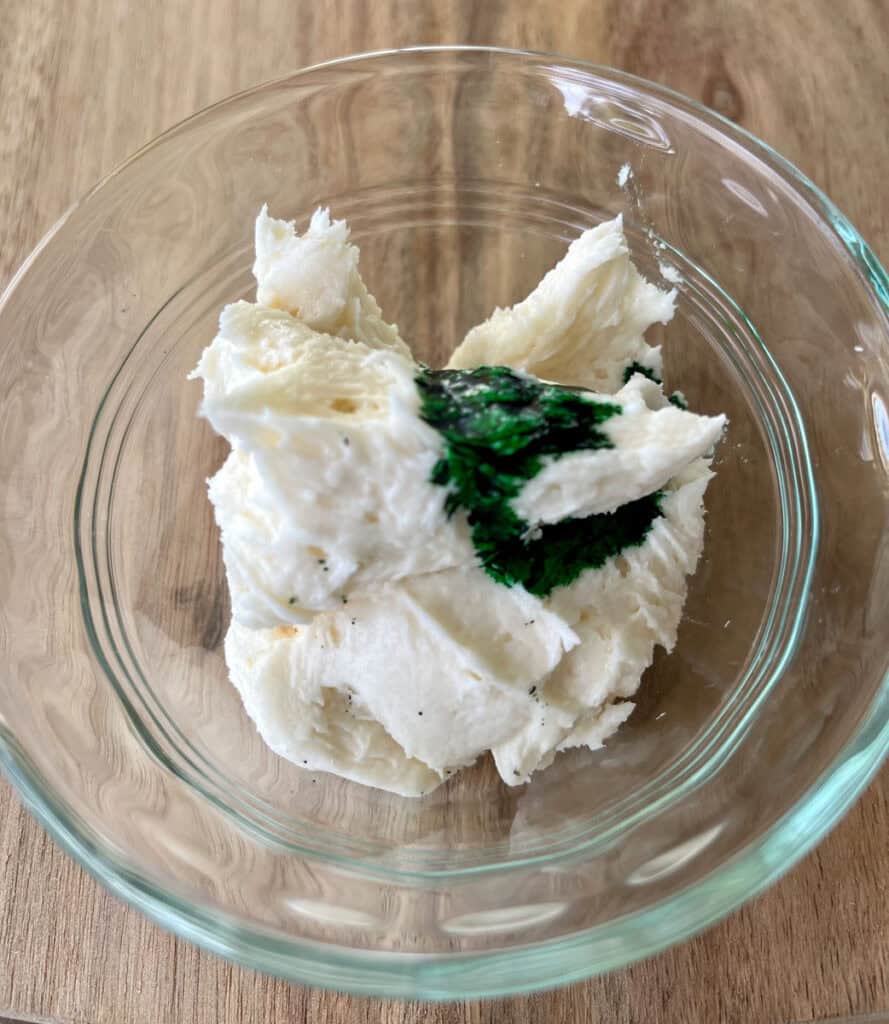 A bowl of cream frosting with green food coloring.