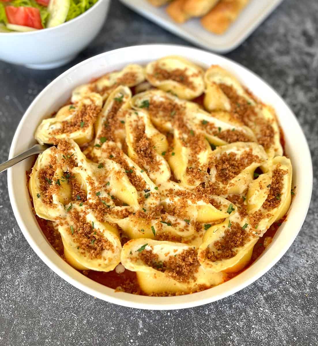 A round dish with large pasta shells filled with cheese and tomato sauce.