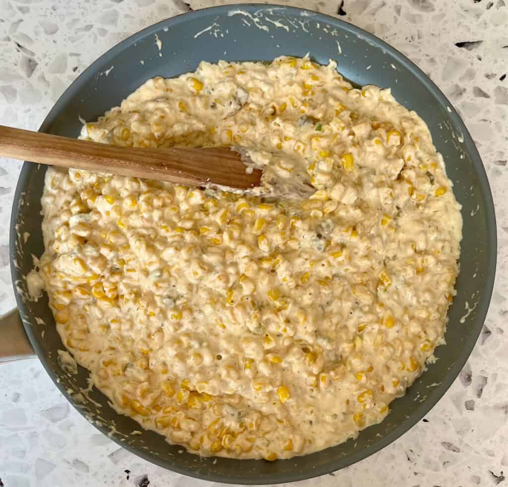A pan filled with corn and cream cheese with a wooden spoon.
