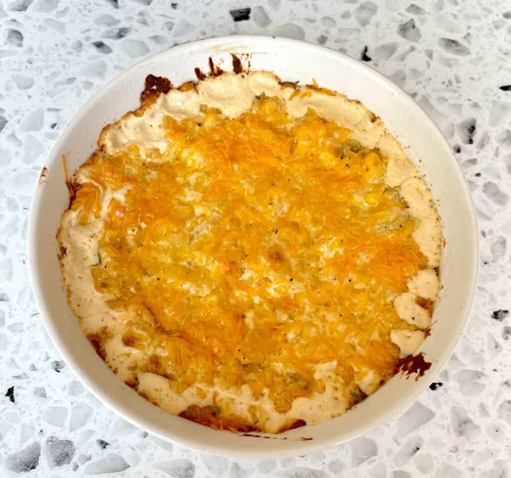 A white dish with baked cheese and corn in it.