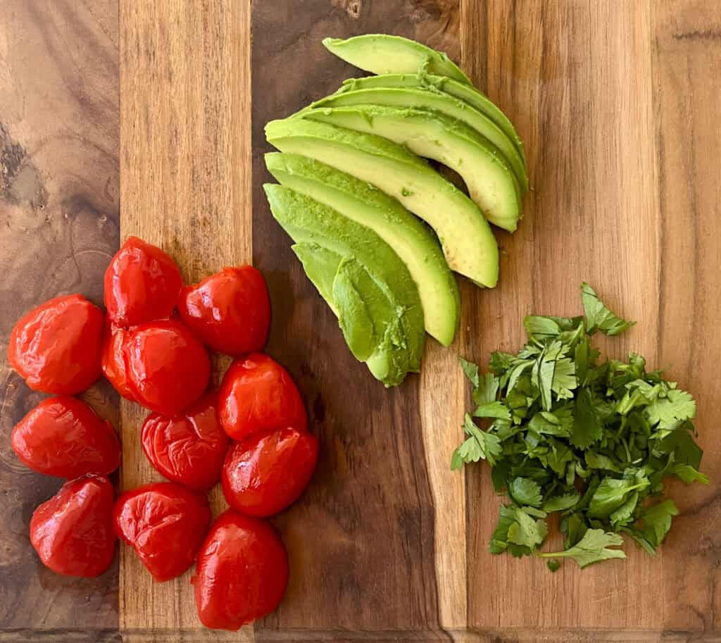 Tomatoes, avocado, and cilantro on a cutting board.