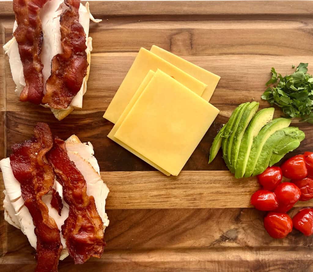 Two sandwiches with bacon, cheese and tomatoes on a cutting board.
