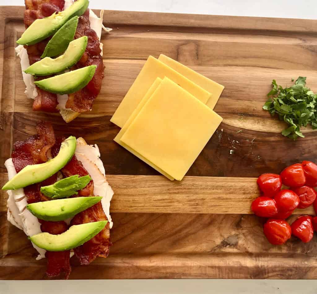 Two sandwiches with bacon, cheese and tomatoes on a cutting board.
