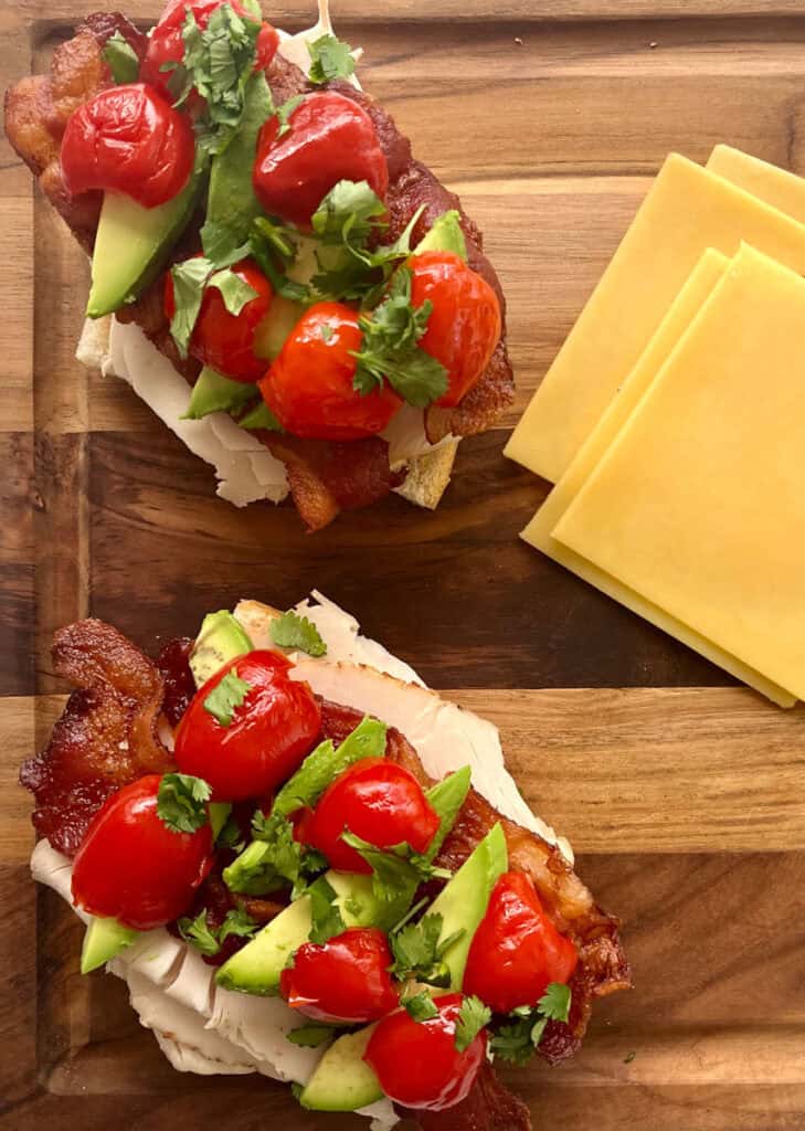 Two sandwiches with bacon, tomatoes and cheese on a cutting board.
