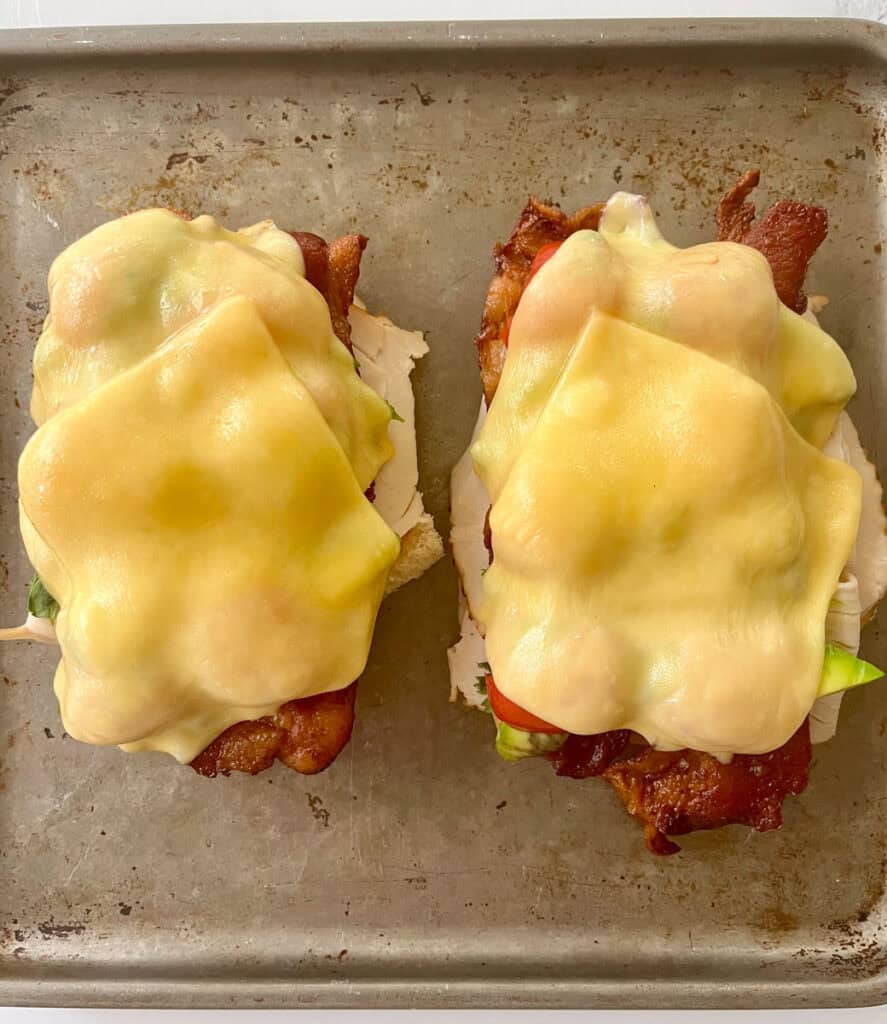 Two open faced sandwiches with cheese and meat on a baking sheet.
