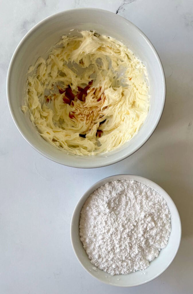 A bowl of white powder and a bowl of butter with cream cheese.