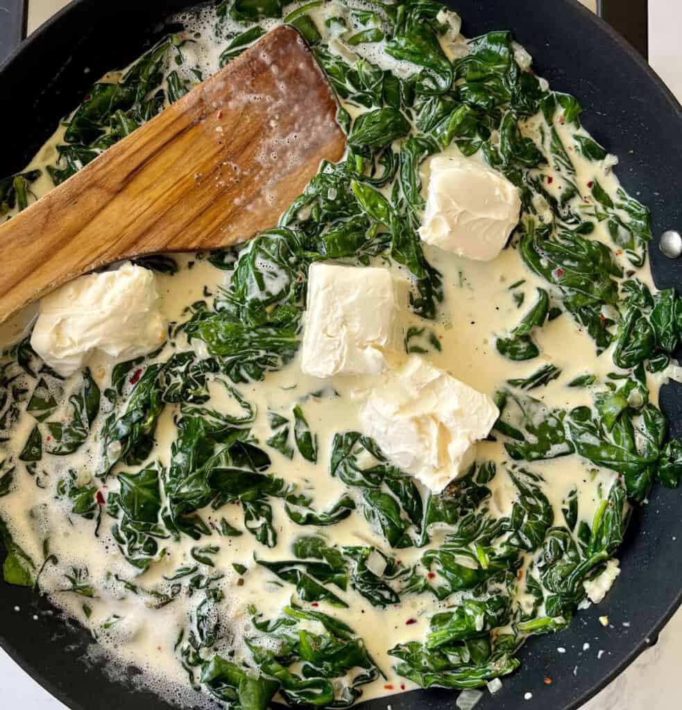 Spinach and cheese in a skillet with a wooden spoon.