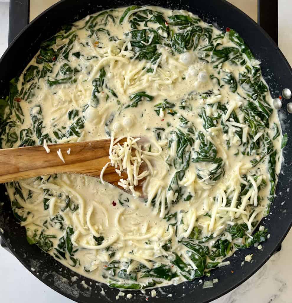A pan filled with cheese and spinach on a stove.