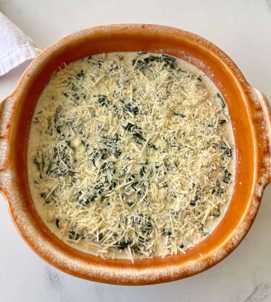 A casserole dish filled with unbaked cheese and spinach.