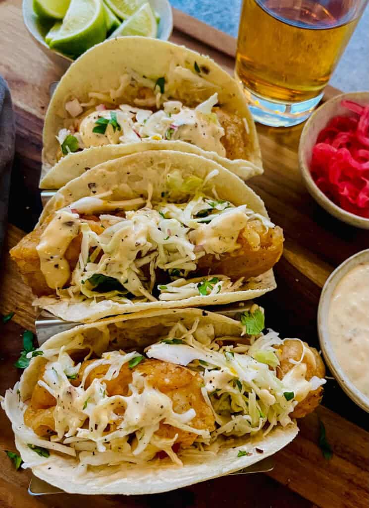 Three tacos on a wooden cutting board.