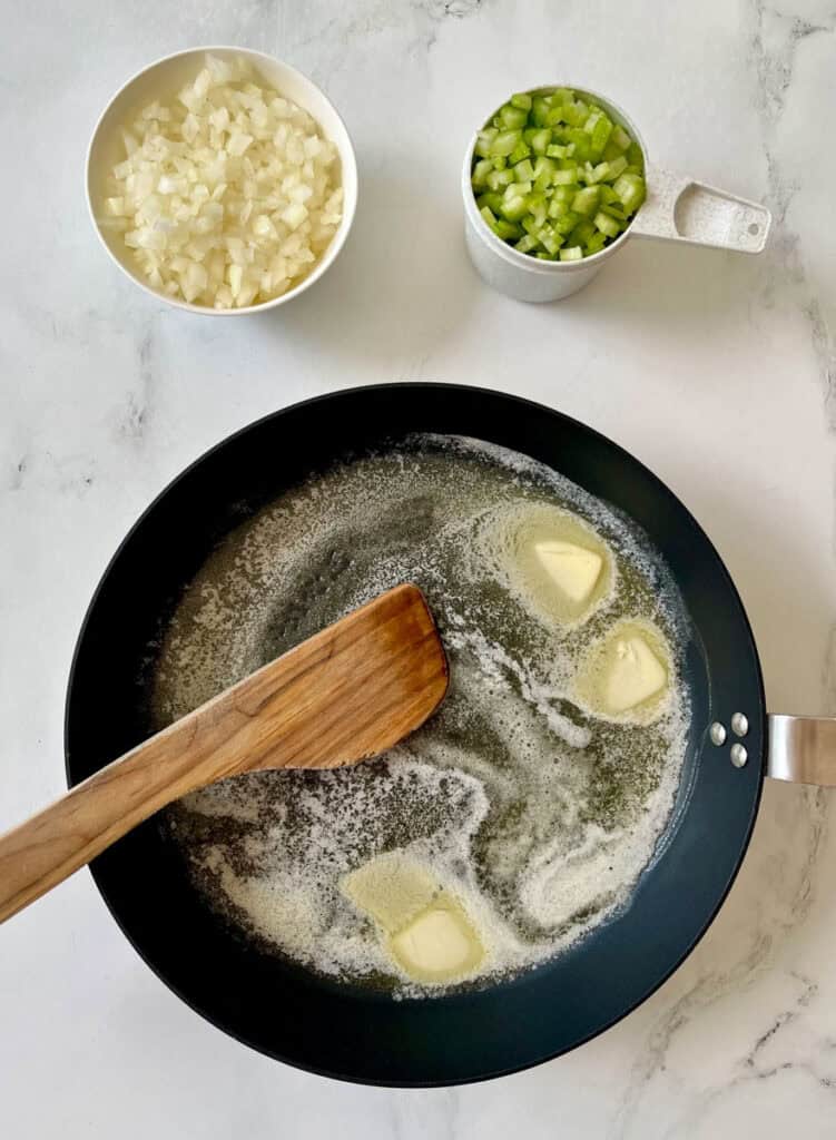 A pan with butter and bowls of onions and garlic on a white counter.
