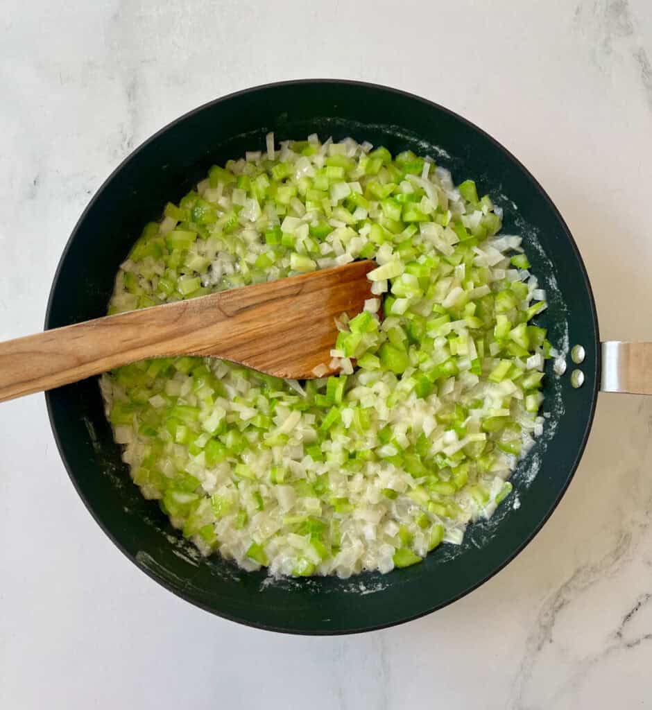 A pan filled with chopped celery and onions and a wooden spoon.