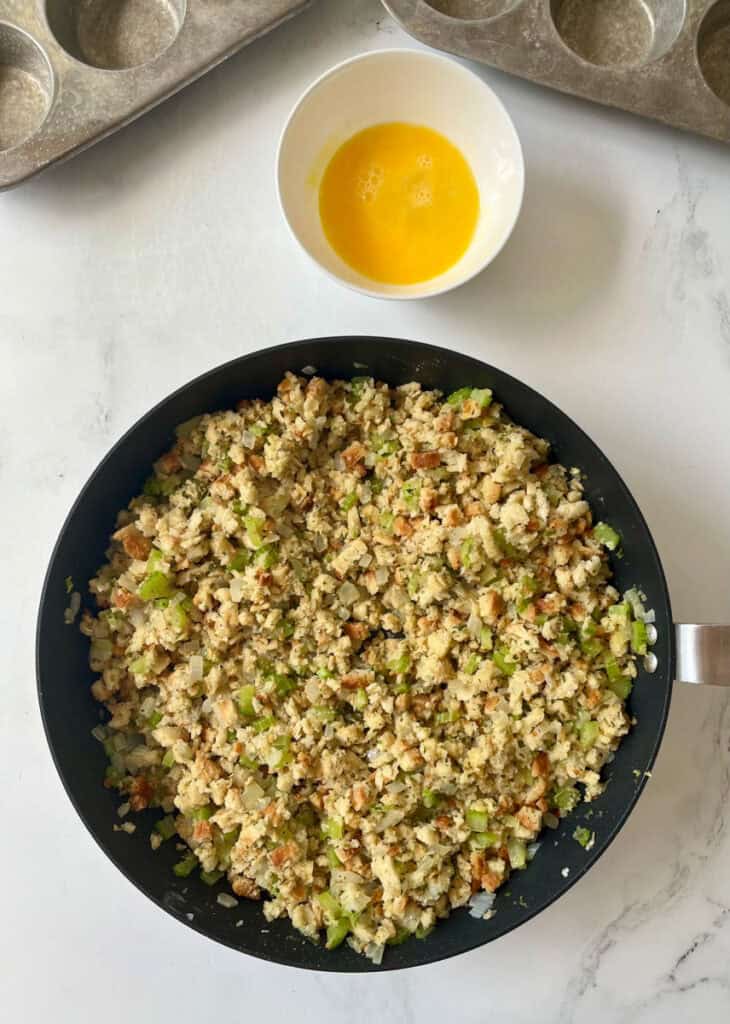 A pan filled with a stuffing mixture next to a bowl of eggs.
