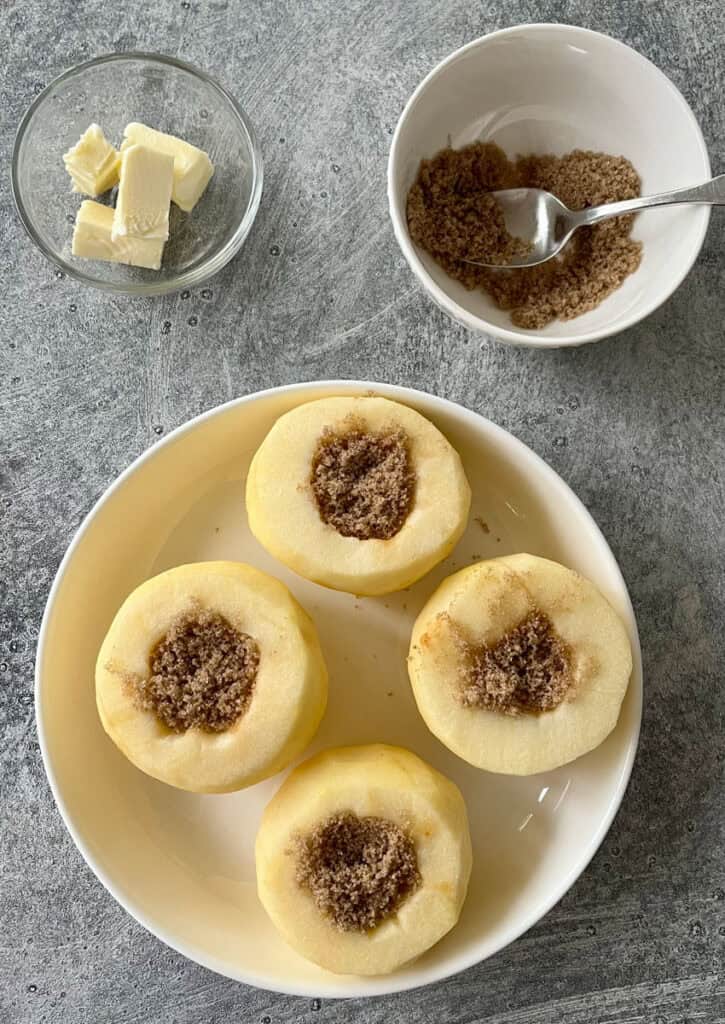 Four peeled and cord apples in a shallow dish with brown sugar in them.