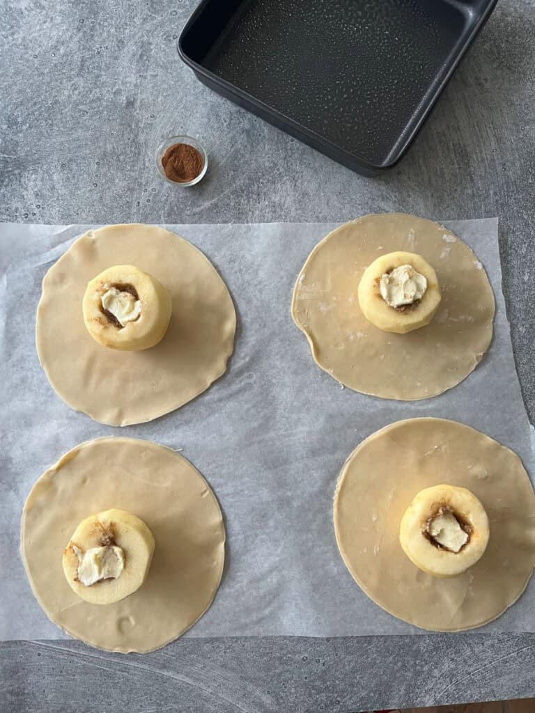 Four apples with rounds of dough with on parchment paper.