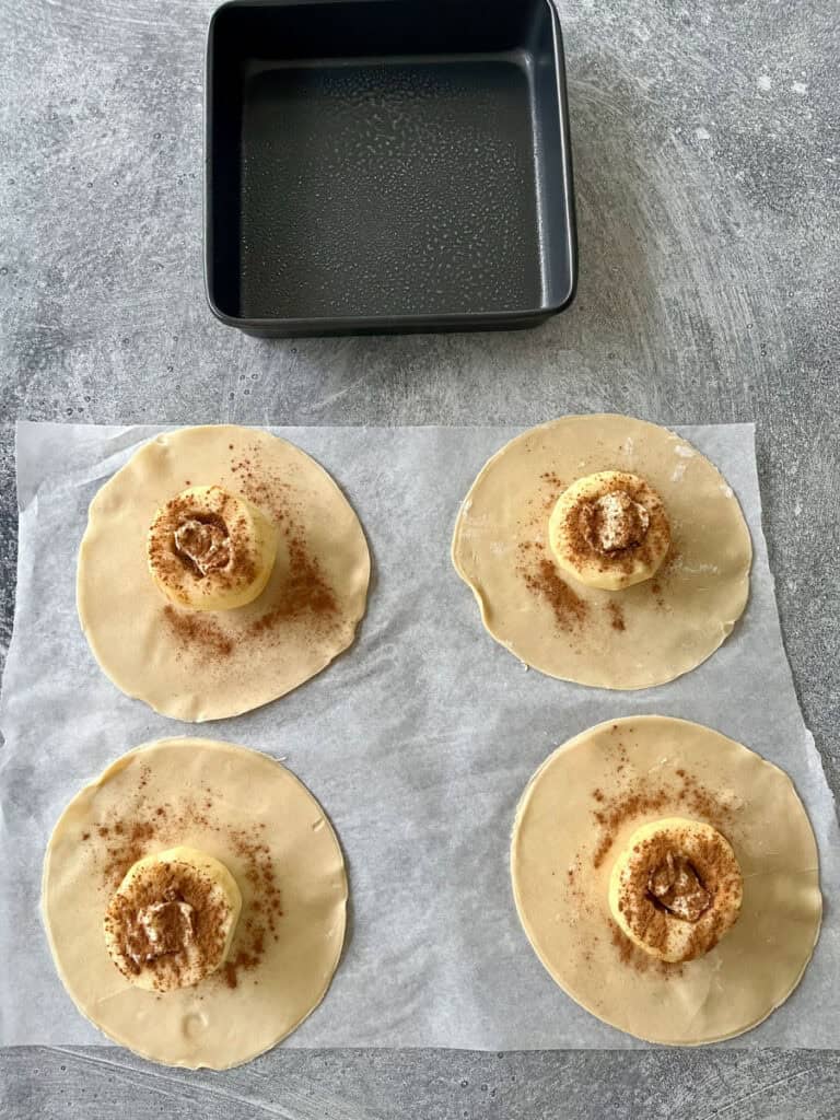 Four apples with rounds of dough with cinnamon on parchment paper.