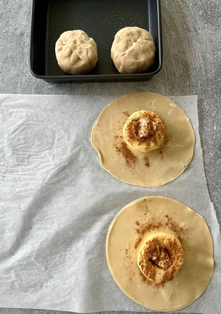 Two apples with rounds of dough with cinnamon on parchment paper.