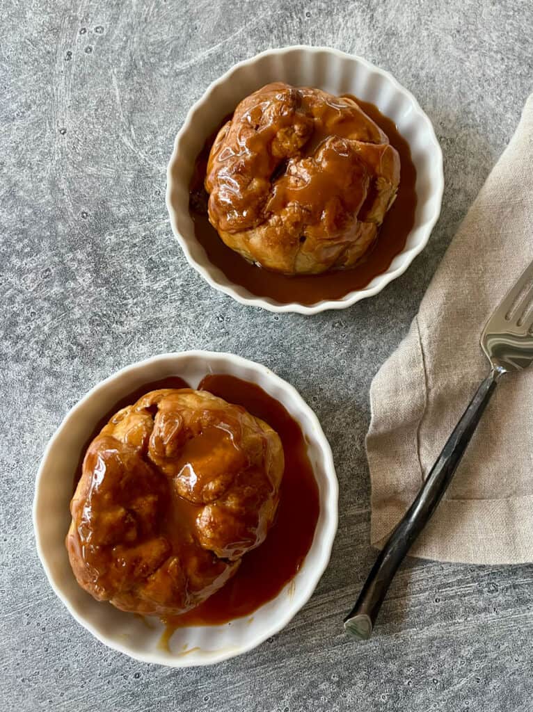 Two small bowls each with a baked apple dumpling with caramel sauce.