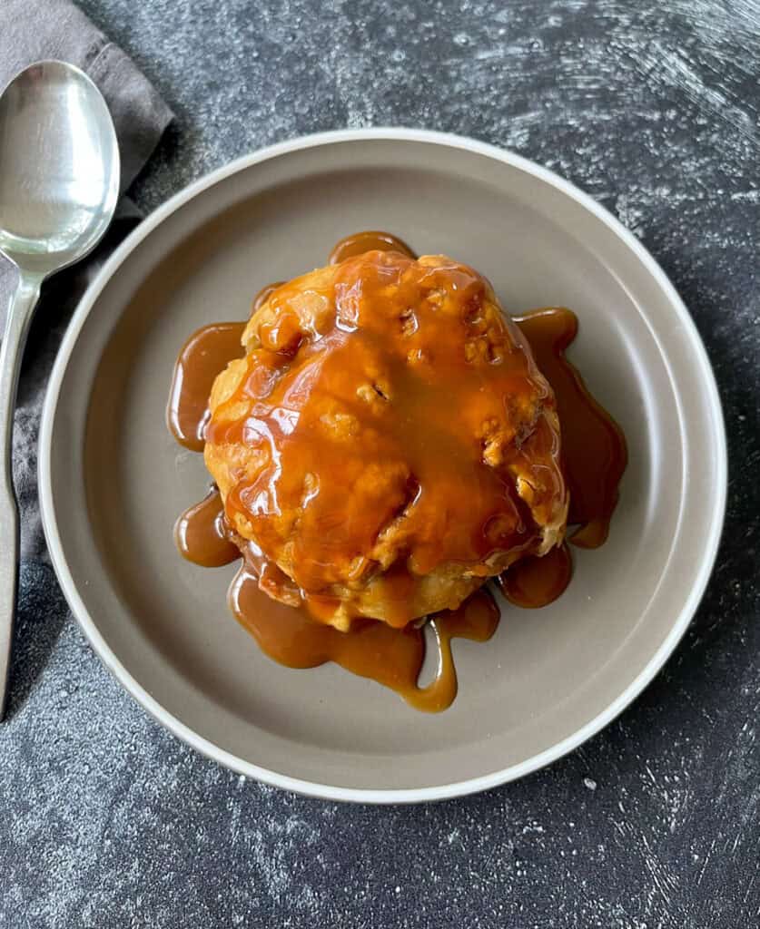 A plate with an apple dumpling with caramel sauce on it.