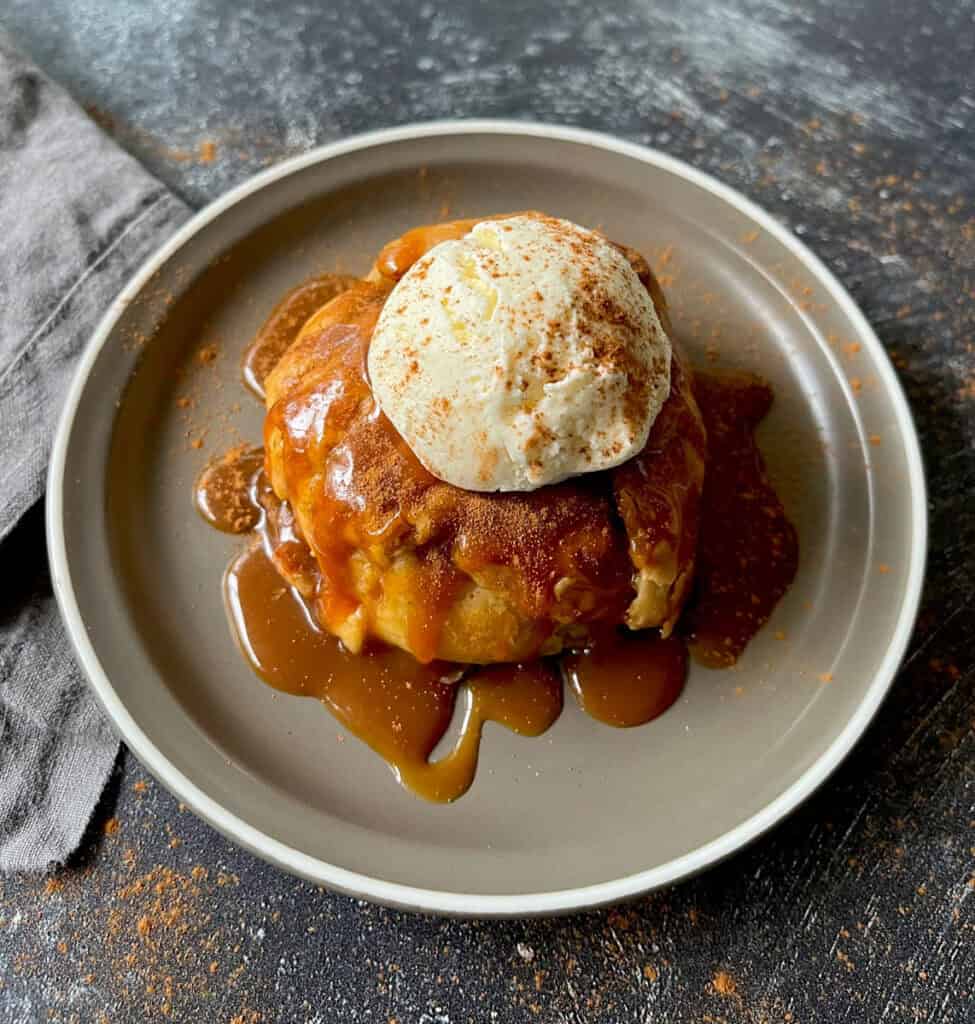 Caramel apple dumpling with ice cream and cinnamon on a plate.