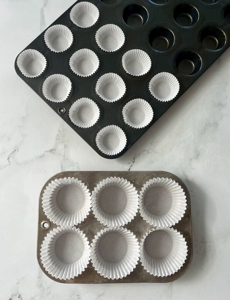 Two muffin tins with different sizes of cupcakes liners.