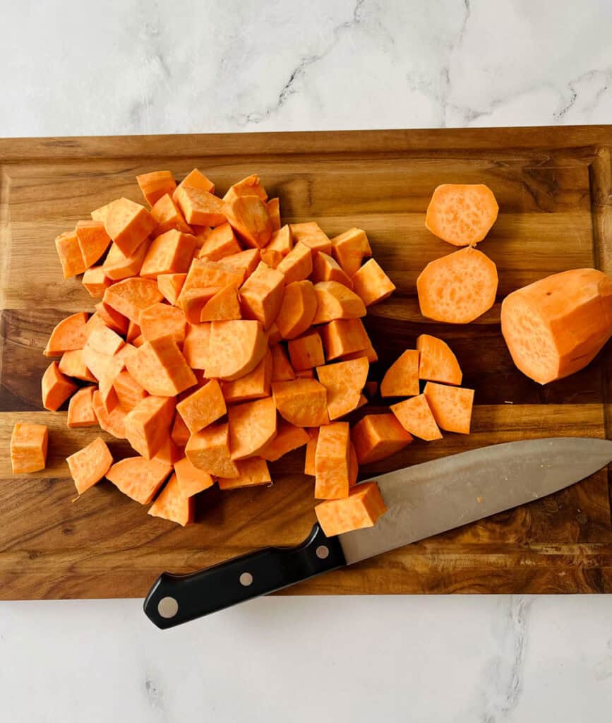 Chopped sweet potatoes on a cutting board with a knife.