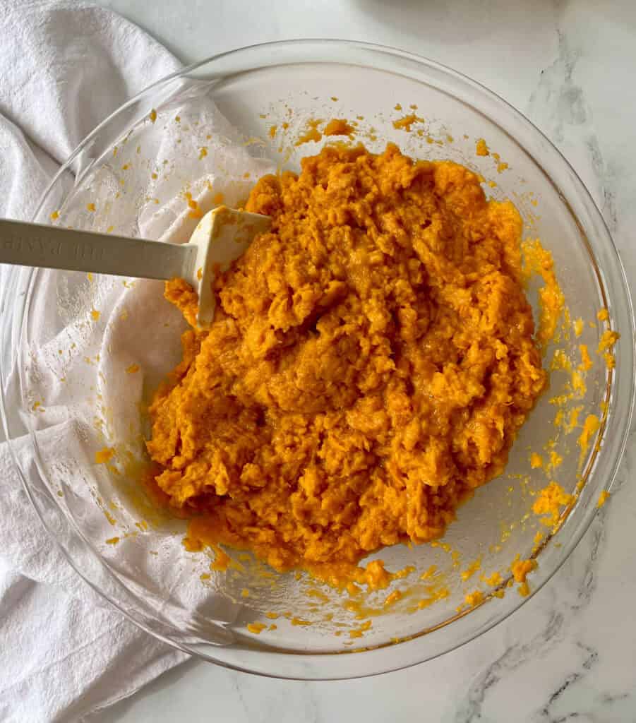 A bowl of mashed sweet potato with a spatula.