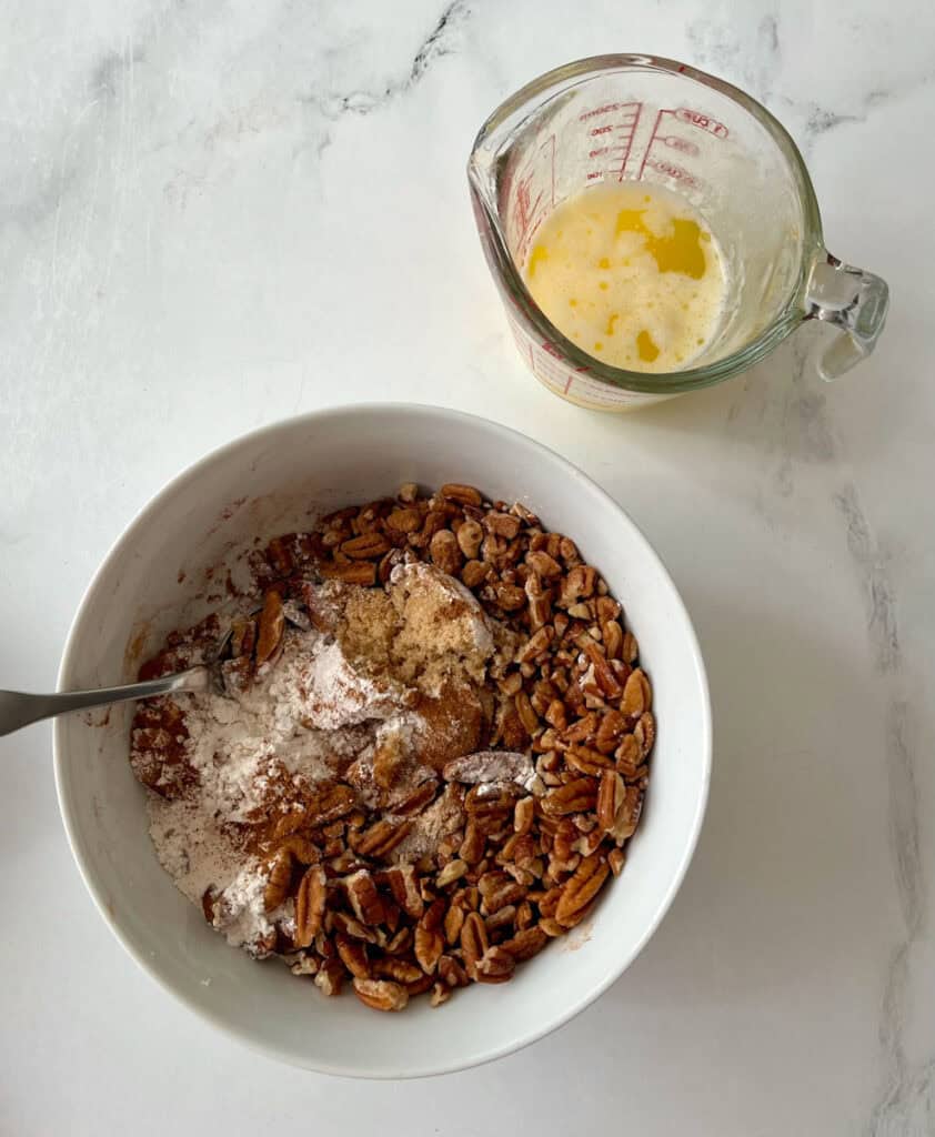 A bowl of pecans and flour, and a measuring cup with melted butter.
